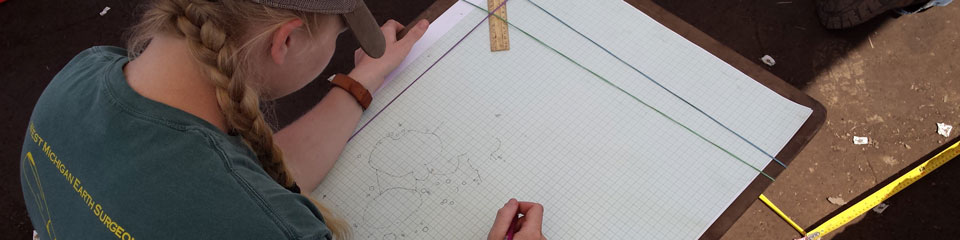 A student sits under a tent in the field while drafting a blueprint.