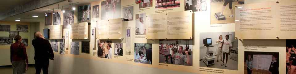 People viewing an informational exhibit with panels of text and photographs on a wall.