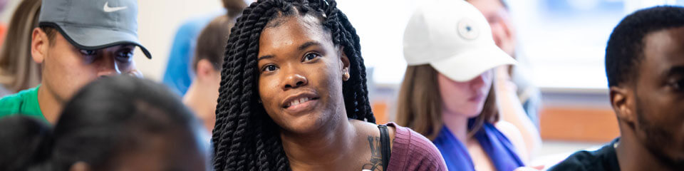 Students seated in a classroom setting, one student with braided hair in focus, engaging with the class.