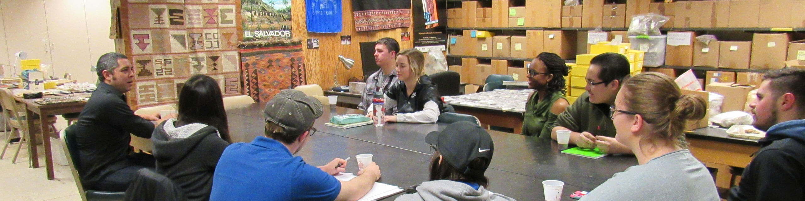 A small anthropology class gathers around a table, listening intently to their professor.