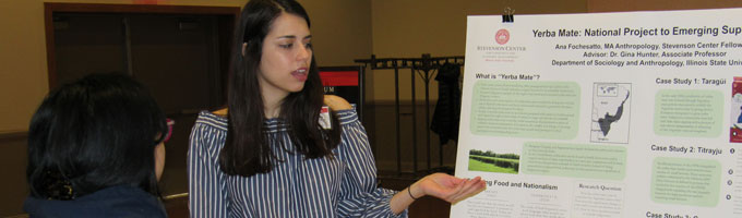 An undergraduate student presents her research poster to a peer.